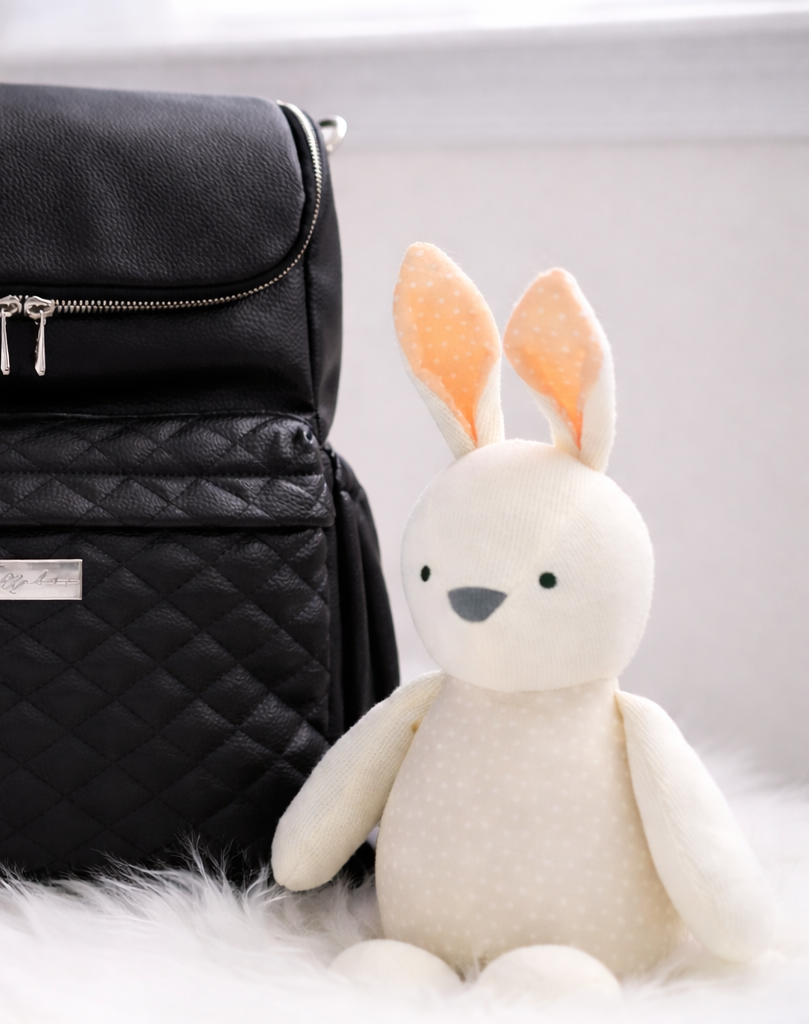 Black quilted diaper bag with a plush bunny toy on a white surface